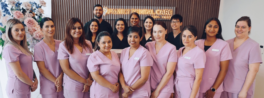 Family Dental care team posing together in front of a Family Dental Care sign, wearing pink and black uniforms