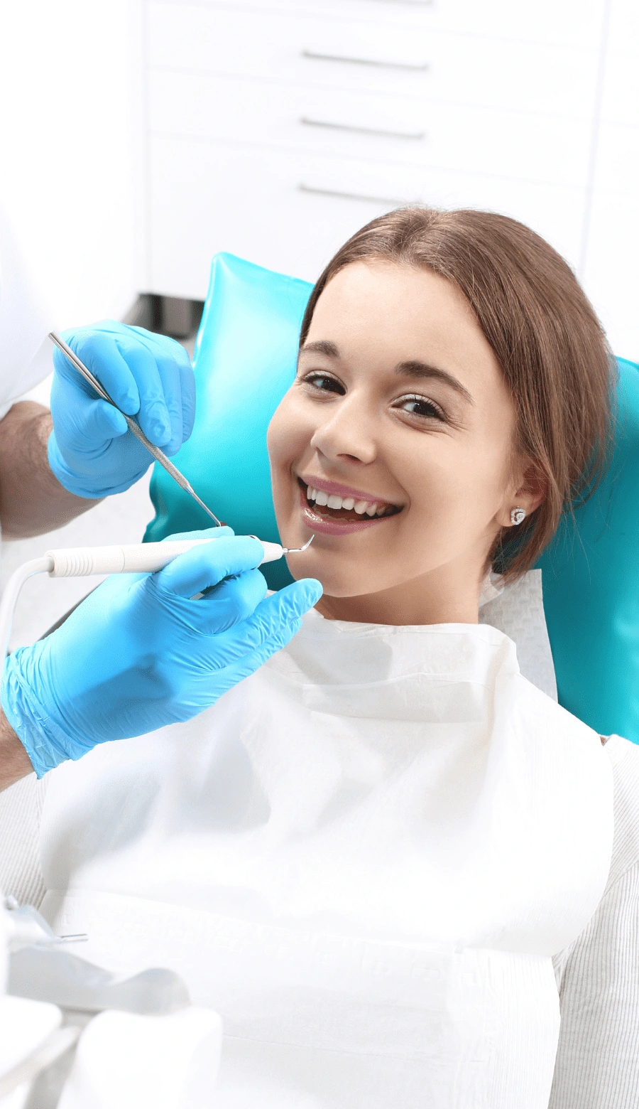 Smiling woman in a dental chair during a checkup as the dentist works with dental tools